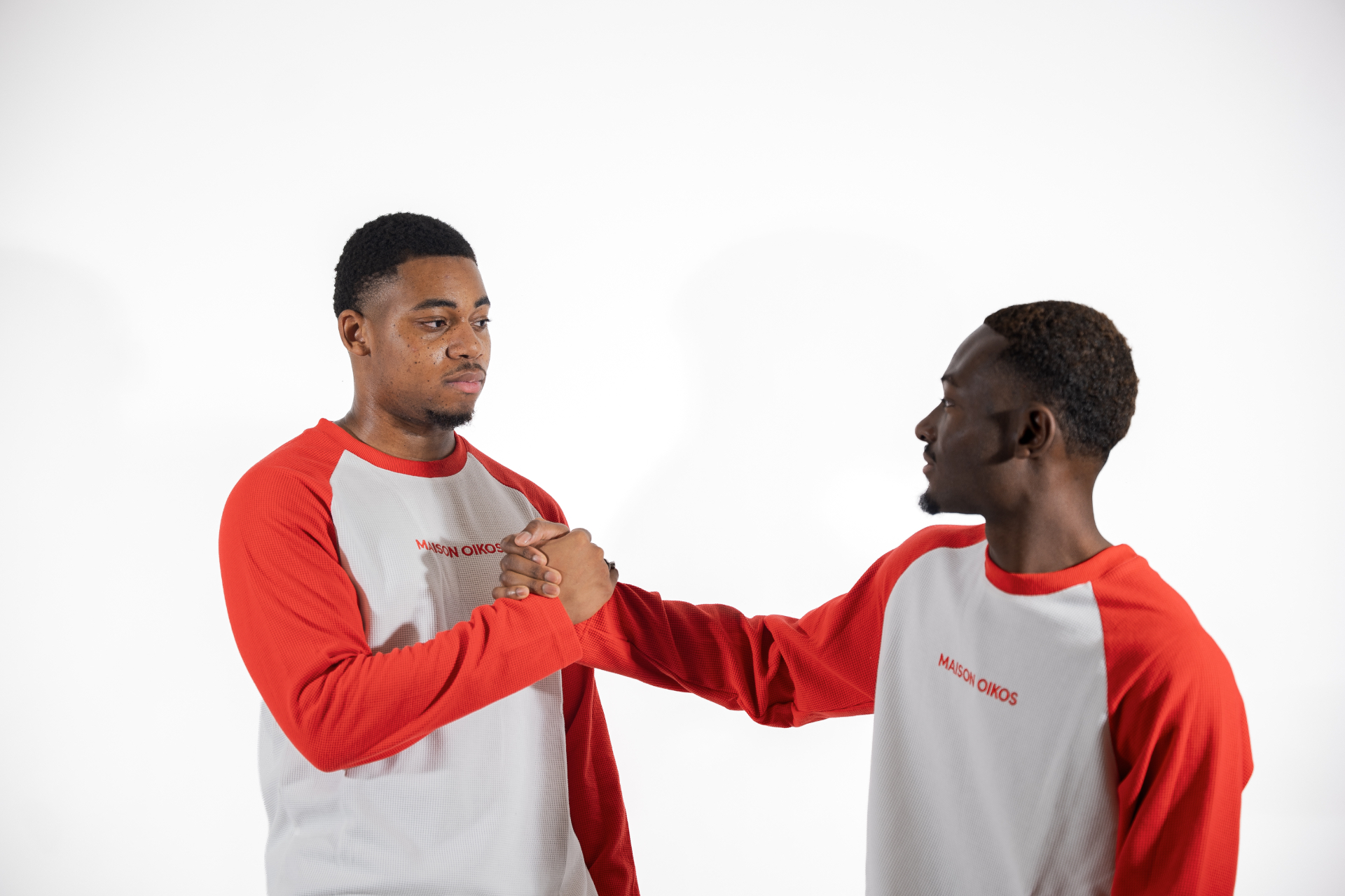 Deux hommes se serrant la main, tous deux en t-shirt raglan blanc et rouge Maison Oikos.