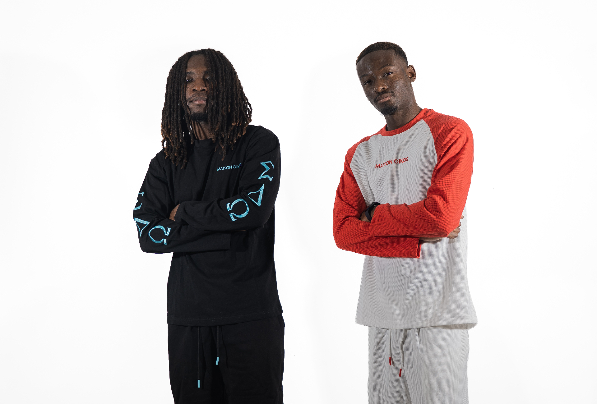 Deux hommes de profil côte à côte, l'un en ensemble noir brodé bleu, l'autre en raglan rouge et gris.