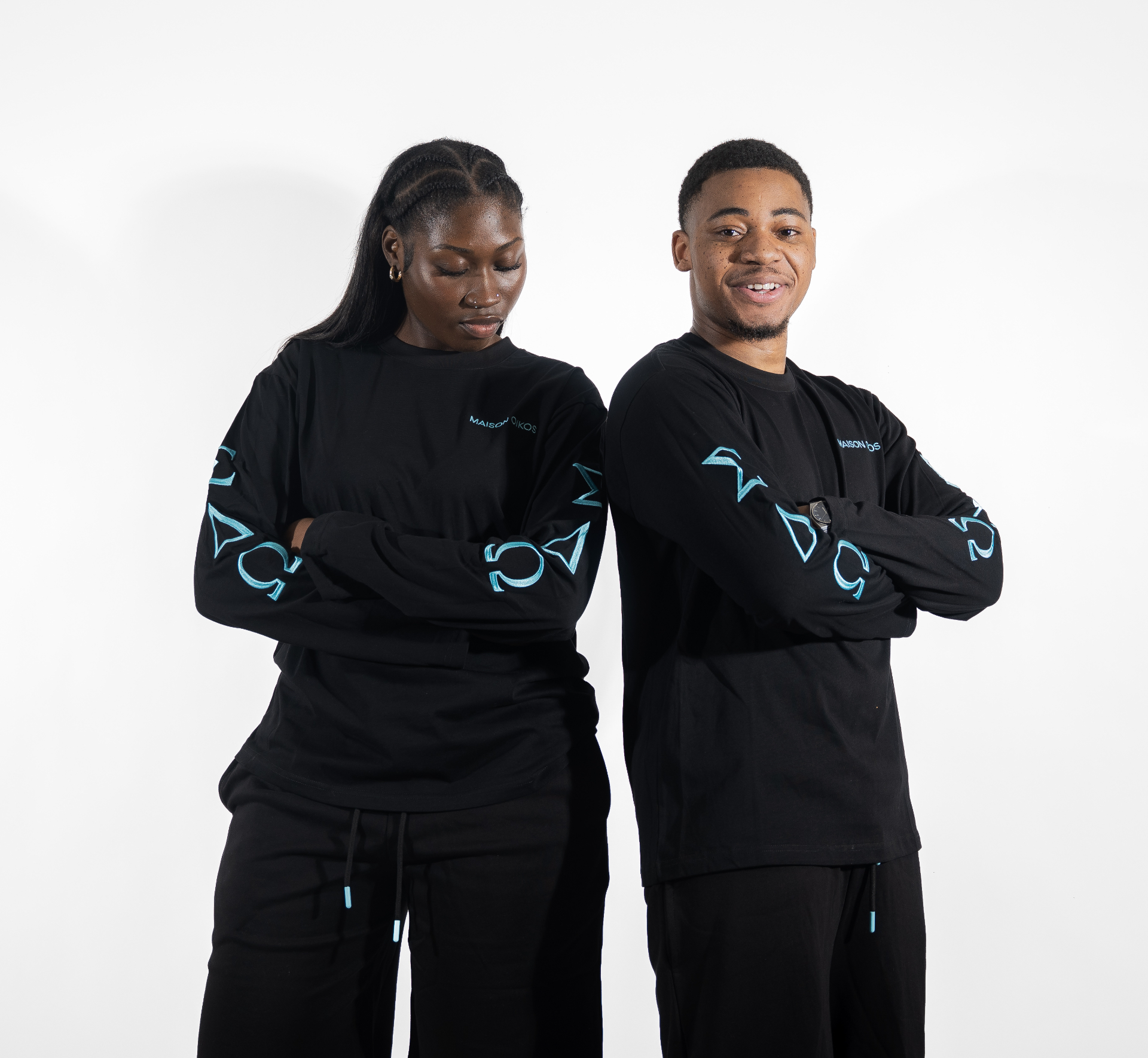 Homme et femme dos à dos, bras croisés, tous deux en ensemble noir Maison Oikos.